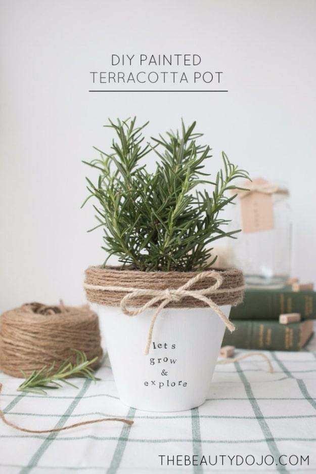 White painted terracotta pot with jute twine tied at the rim and stamped lettering, planted with a rosemary plant