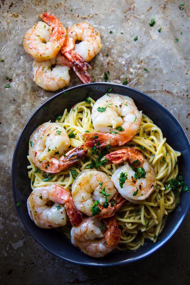 Gluten free shrimp scampi with spaghetti, whole cooked shrimp and chopped parsley in a dark blue bowl