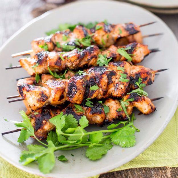Beer and honey BBQ chicken skewers on a white plate, charred at the edges and scattered with cilantro