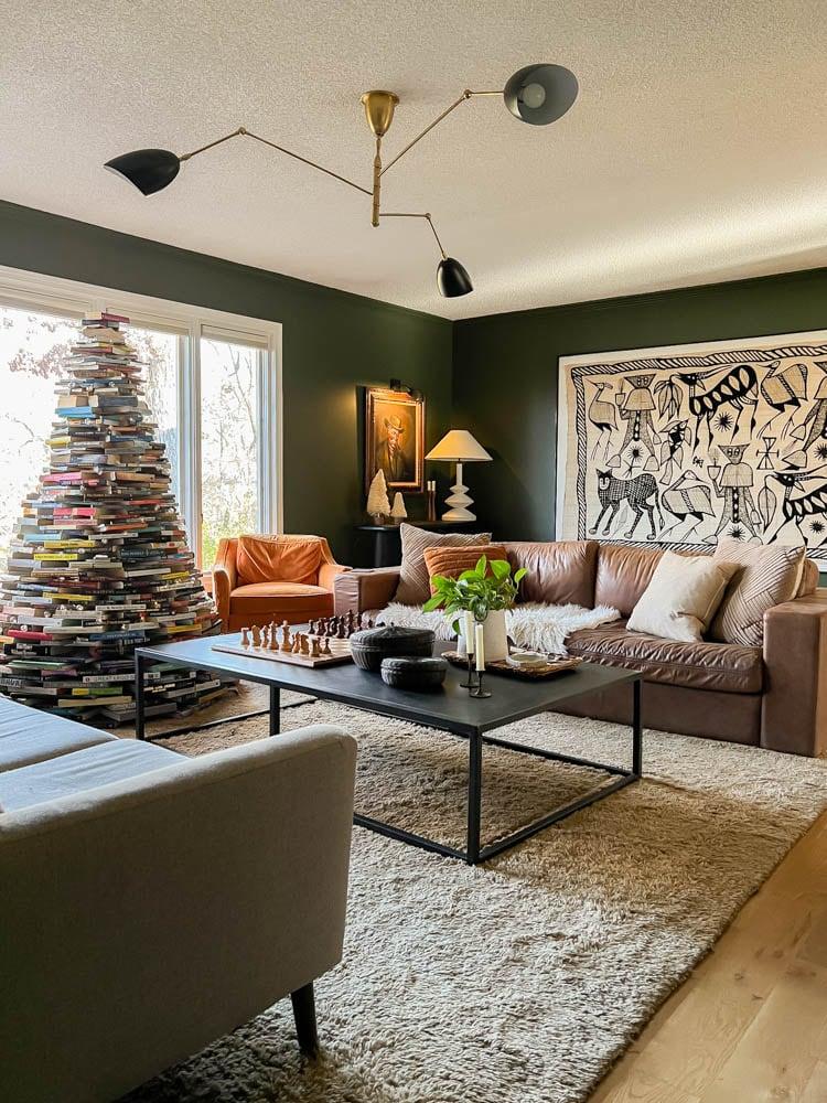Six foot Christmas tree built from hundreds of stacked books tapering to a point, wrapped in string lights in a living room