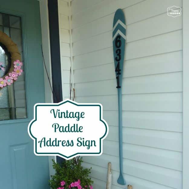 Vintage wooden paddle painted teal with white painted arrows and iron house numbers, hung on a porch wall