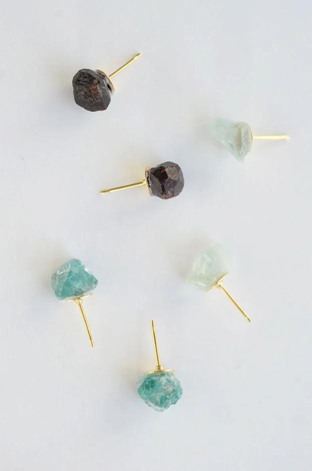 DIY raw stone earrings, six rough amazonite and garnet stones glued onto gold posts, scattered on a white surface
