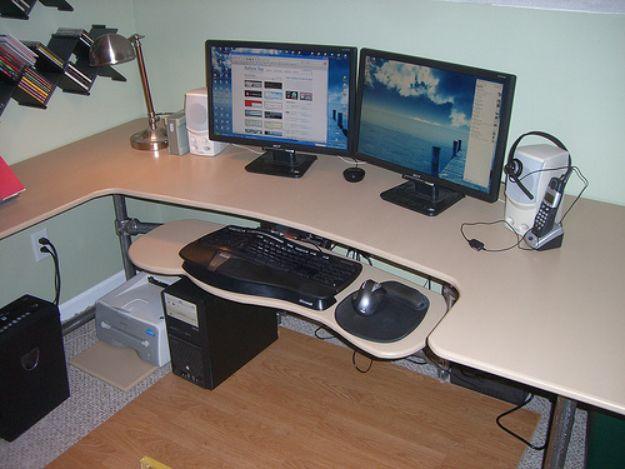 Corner desk on a metal pipe frame holding two monitors, a lamp and a headset, with a pull out keyboard tray