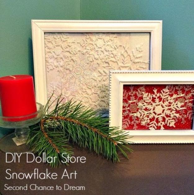 Two white picture frames holding white snowflakes on cream and red glitter paper beside a red candle
