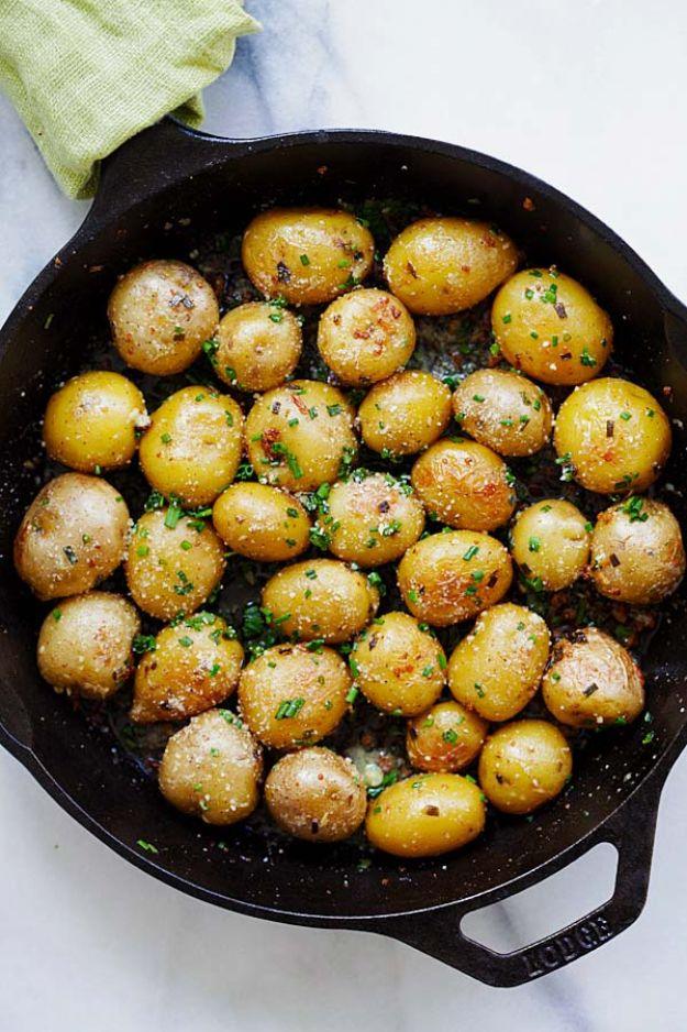Cast iron skillet of small whole roasted potatoes coated in herb butter beside a green linen kitchen napkin