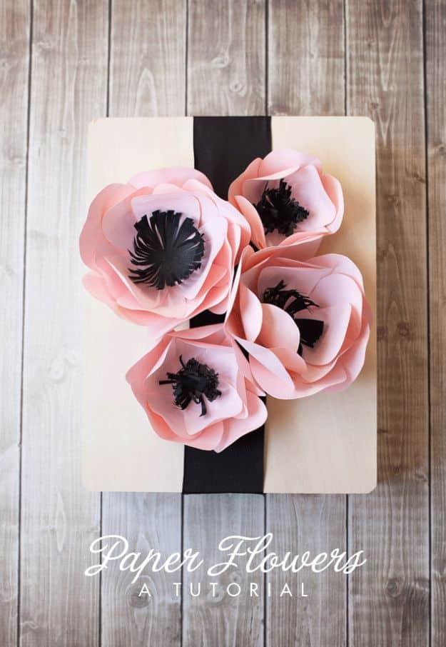 Simple paper flowers, four pale pink paper flowers with black centers glued to a wooden board and ribbon