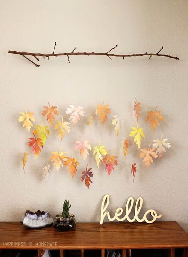 Watercolor paper leaf mobile with painted autumn leaves hanging on threads from a branch above a wood console