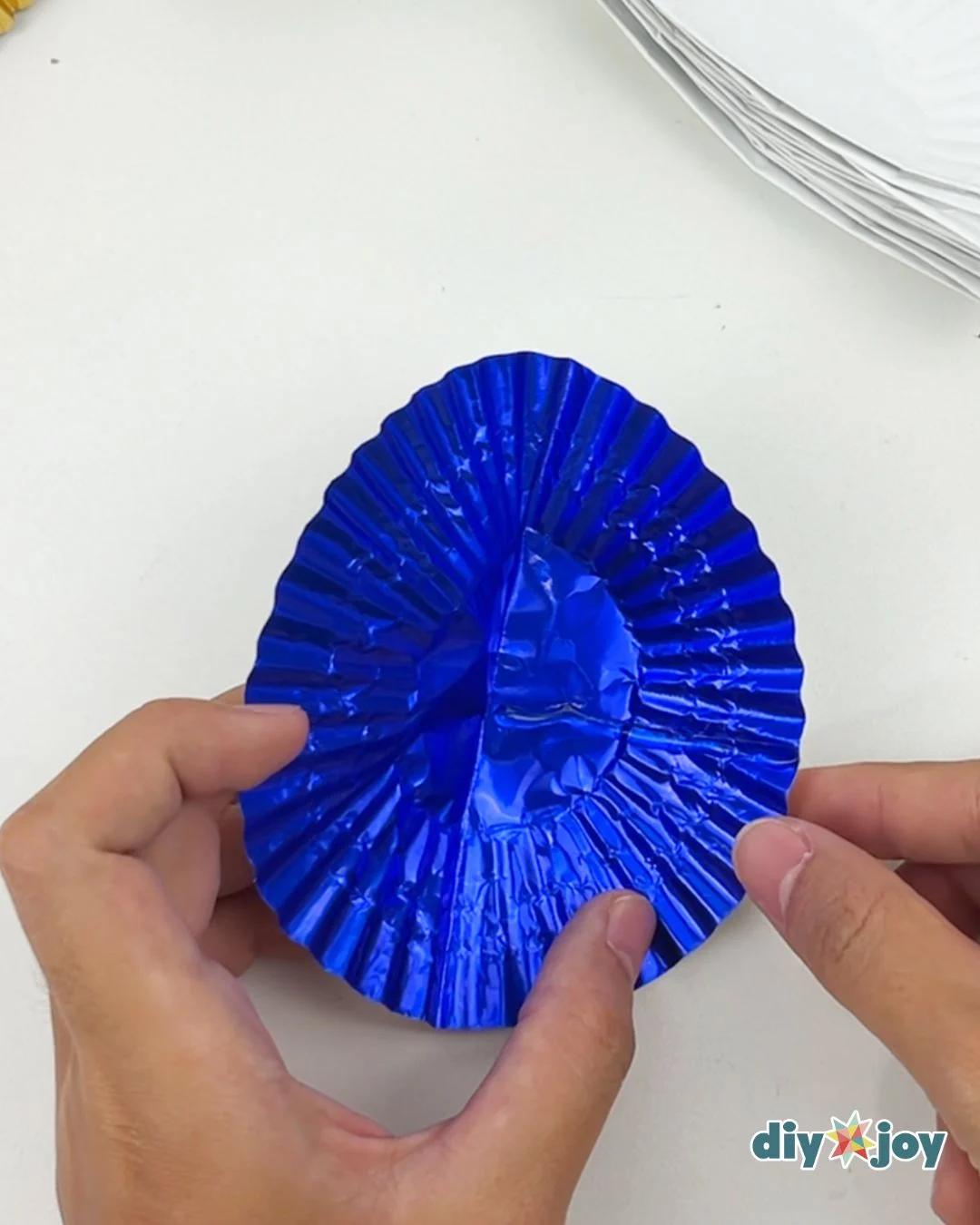 Cheap DIY - a creased blue metallic cupcake liner held open between two hands with a stack of white liners nearby
