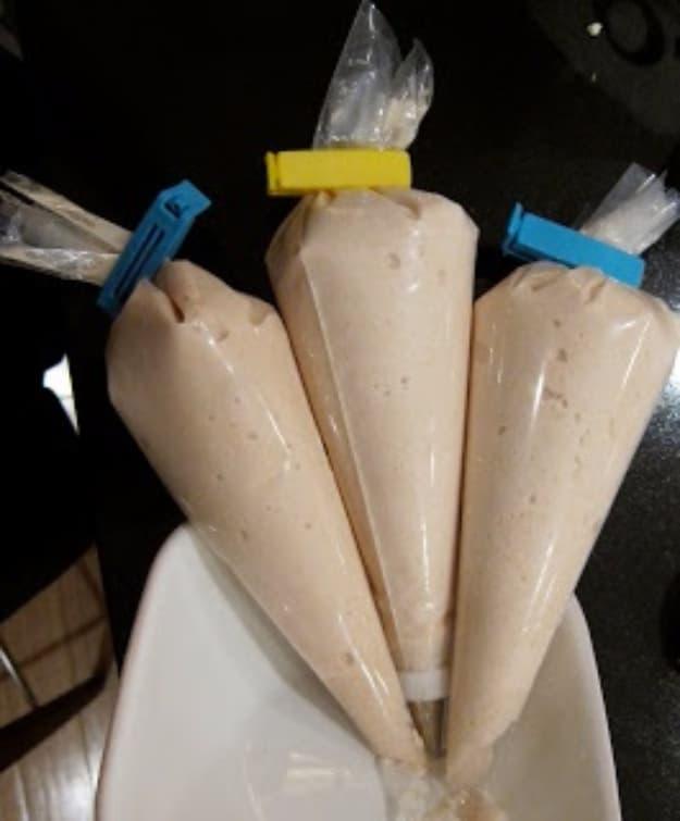 Three clear bags of pancake batter clipped shut and standing point down in a white dish on a dark table