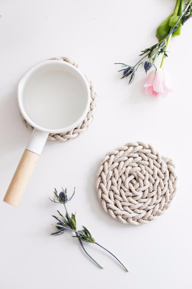 Coiled natural rope trivet finger knitted into a spiral, beside a white enamel milk pan and dried blue thistles