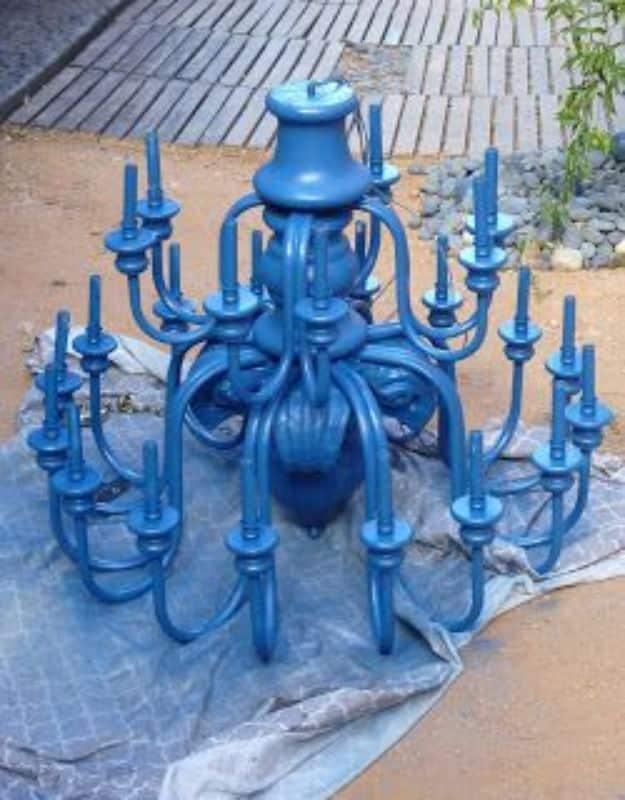 Large royal blue spray painted chandelier with twenty four candle arms sitting on a drop cloth outdoors before hanging