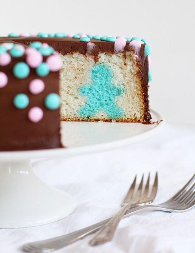 Slice of gender reveal cake showing a blue baby silhouette inside white cake with a chocolate shell and dots