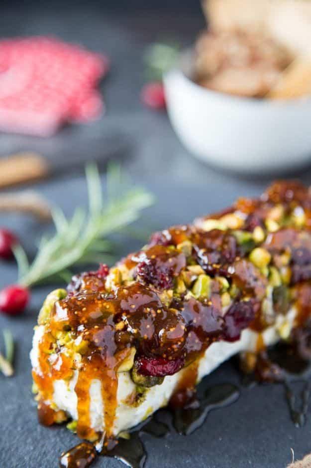 A goat cheese log rolled in chopped pistachios and drizzled with honey and fig spread on a dark stone board