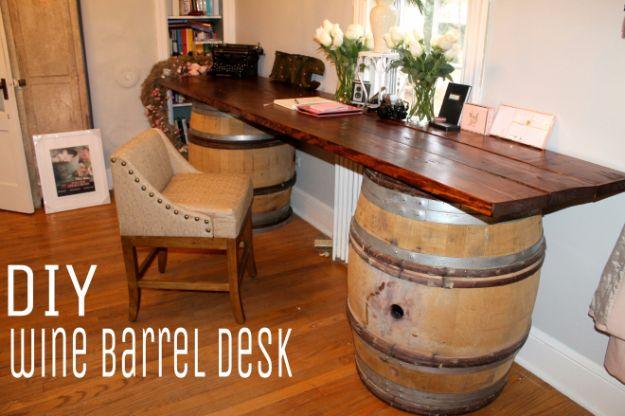 DIY rustic wine barrel desk, a long stained plank top resting on two oak wine barrels against a white wall with a chair