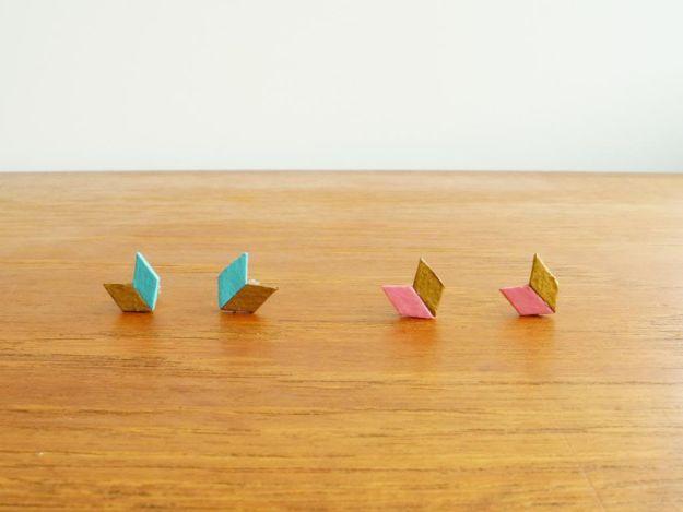 Two tone chevron stud earrings made from painted cardboard diamonds in teal and gold and pink and gold on a wood table