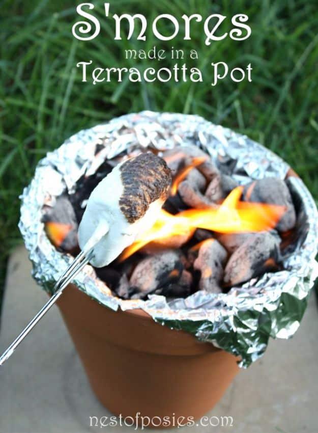 Foil lined terracotta pot full of glowing charcoal with a marshmallow stick, under a typeset S'mores title