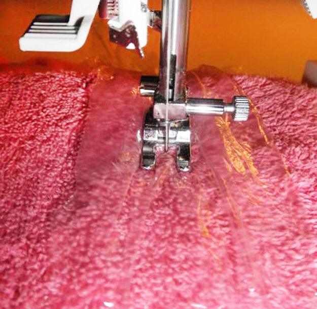 Plastic grocery bag as stabilizer, a presser foot stitching through clear plastic laid over deep red terry towelling
