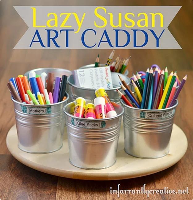 Three labeled galvanized pails of markers, glue sticks and colored pencils on a wooden lazy susan turntable