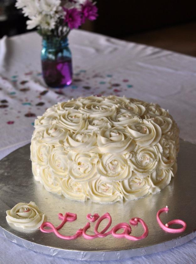 White rosette piped birthday cake covered in swirled buttercream roses with a child's name written in pink