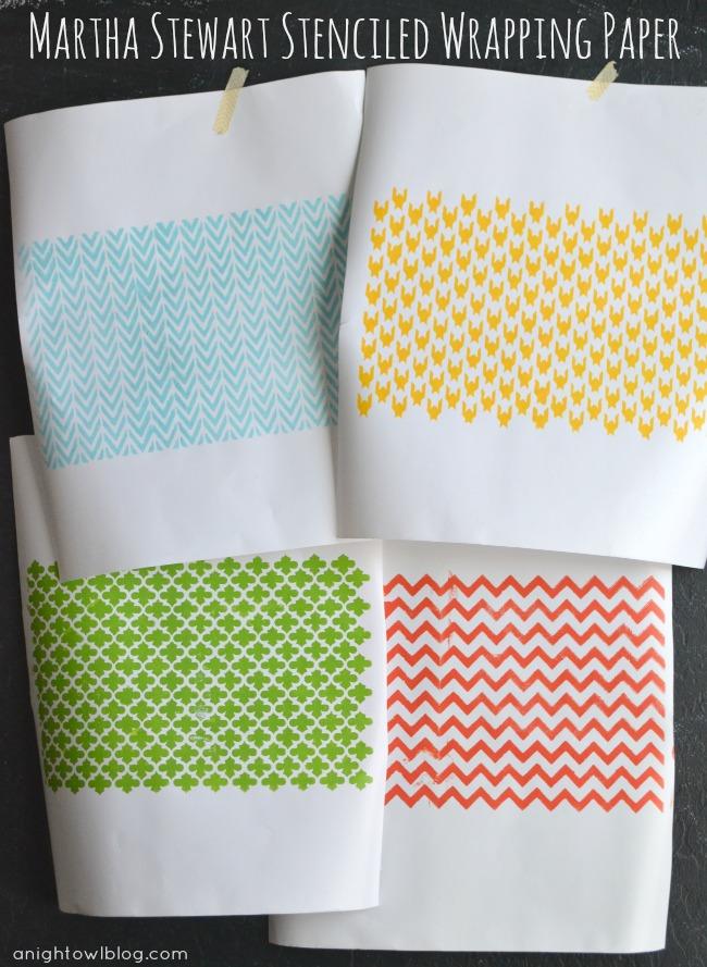 Four sheets of white wrapping paper hand stenciled in aqua, yellow, green and orange taped to a dark wall