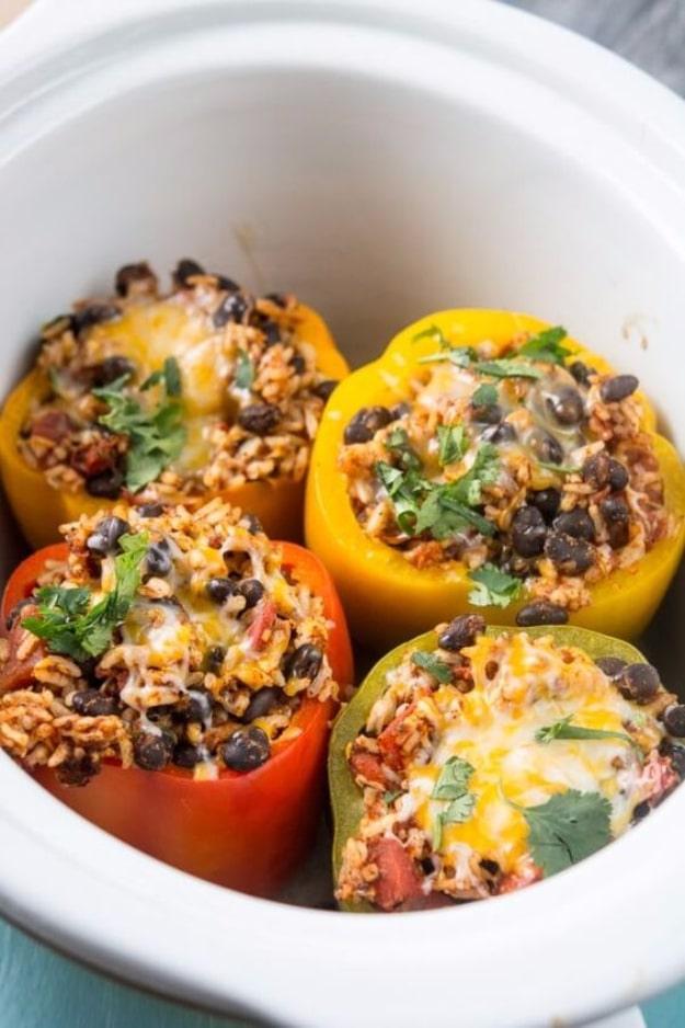 Four slow cooker stuffed peppers filled with rice, black beans, tomatoes, cheese and cilantro in a white crockpot
