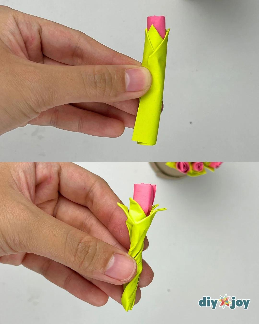 Close up of a hand wrapping a lime green fringed sticky note around the base of a rolled paper rose flower
