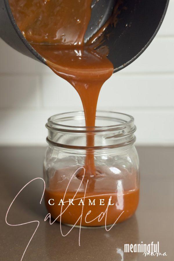 Salted caramel sauce pouring from a dark saucepan into a glass mason jar on a counter, with script title text