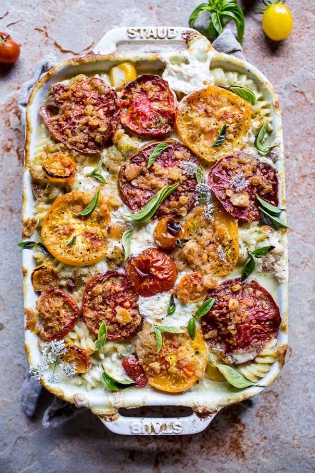 Caprese mac and cheese in a dark grey Staub dish topped with red and yellow roasted tomato slices and basil