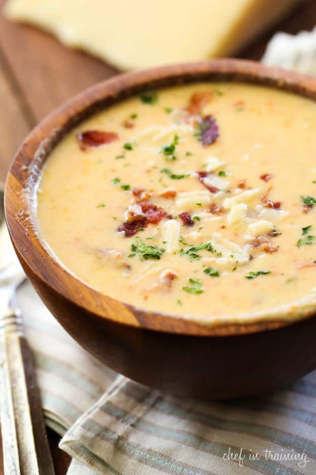 Asiago bisque in a dark wooden bowl, thick and pale gold with crumbled bacon and chopped parsley on top