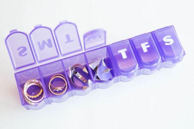 Purple weekly pill organizer with rings and earrings in its compartments, lids labeled S M T W T F S