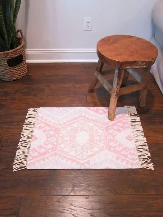Pink and cream kilim pattern DIY rug with white fringed ends on dark wood floor beside a rustic wooden stool