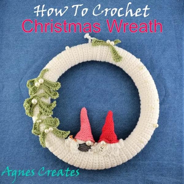 A cream crocheted wreath with two small crocheted gnomes in pink and red hats and crocheted mistletoe with pearl berries