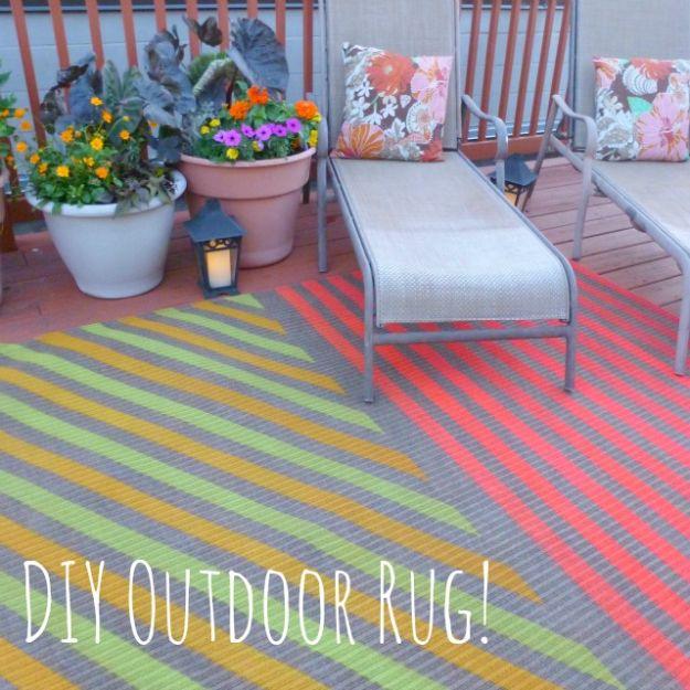 DIY outdoor rug spray painted in green, yellow, coral and grey stripes on a roof deck with planters and a lounger