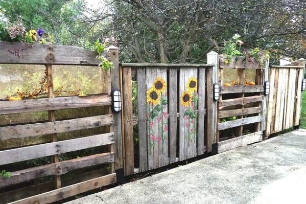 Pallets patio fence, a weathered pallet fence painted with sunflowers standing along a concrete patio edge with wall lights