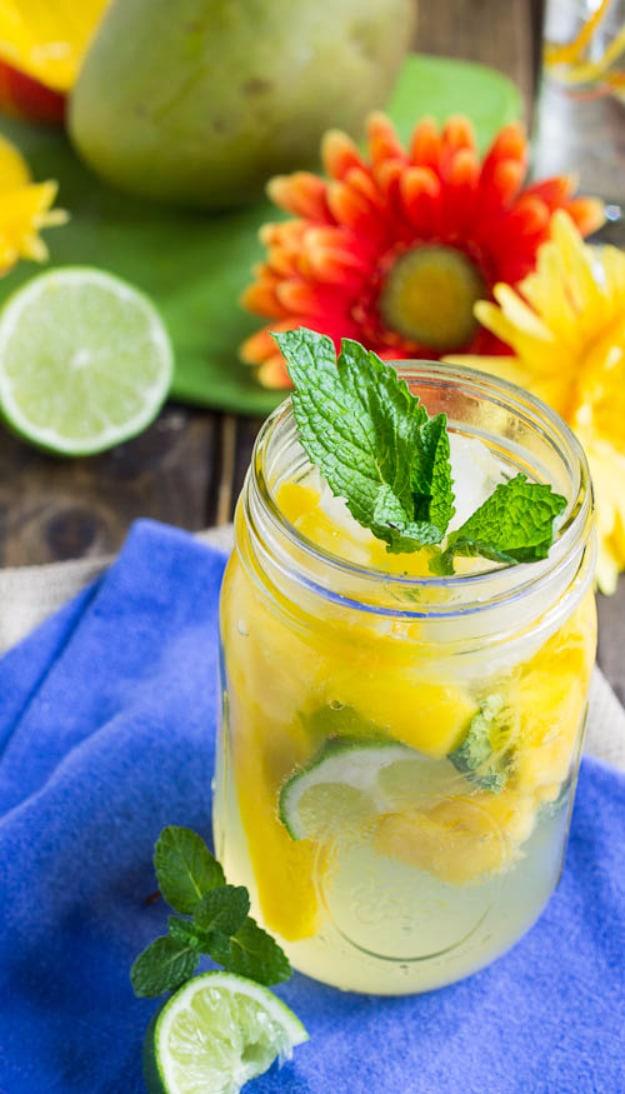 Mango mojito in a mason jar with mint leaves and lime slices, whole mango and a flower behind the glass