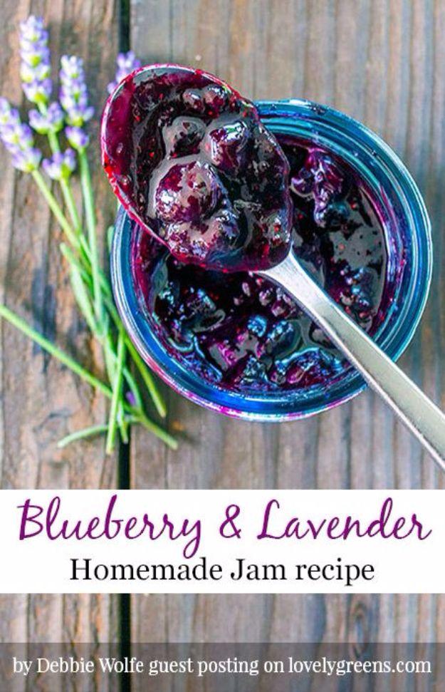 Spoonful of dark blueberry lavender jam lifted from a blue jar with fresh lavender stems on grey wood