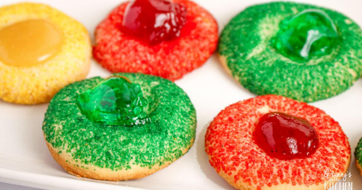 Thumbprint cookies rolled in red, green and yellow sanding sugar with matching jelly and lemon curd centers on a white plate