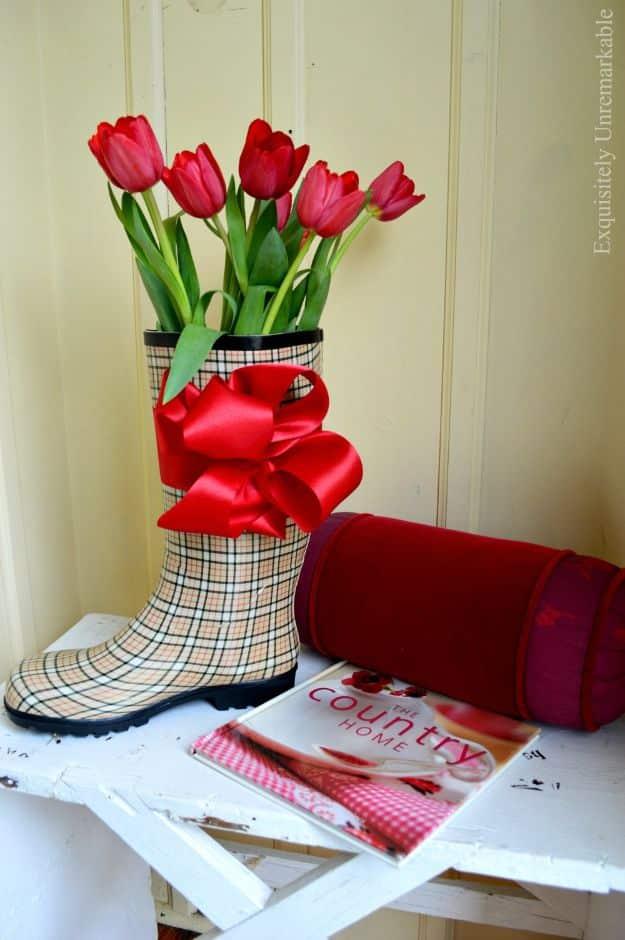 Rubber rain boot decor, a plaid rain boot filled with red tulips and tied with a red bow on a white bench
