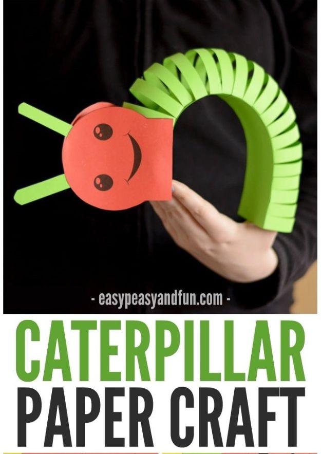 Red paper caterpillar with layered green paper strips and a drawn cartoon face, held up on an adult's hand