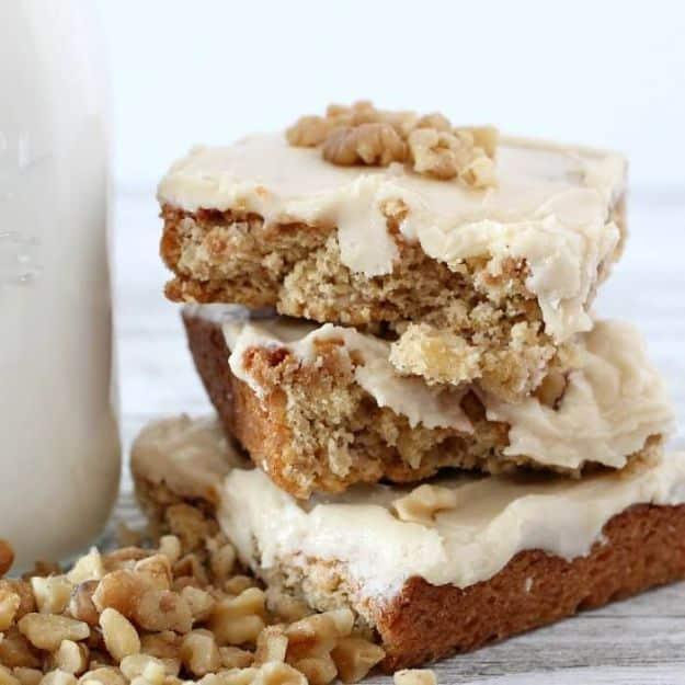 Three thick golden butterscotch bars stacked with pale frosting and walnuts, beside a glass milk bottle