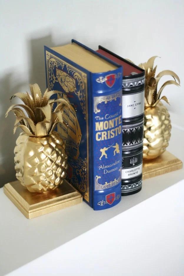 Easy pineapple DIY bookends, two gold spray painted faux pineapples on square wood blocks holding classic hardback books