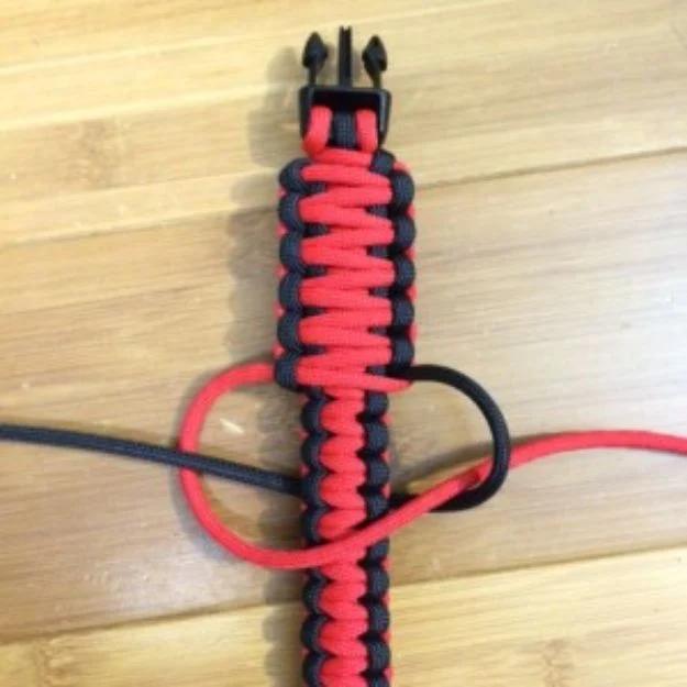 King cobra paracord bracelet part woven in red over black cord, laid out flat on a pale wooden board