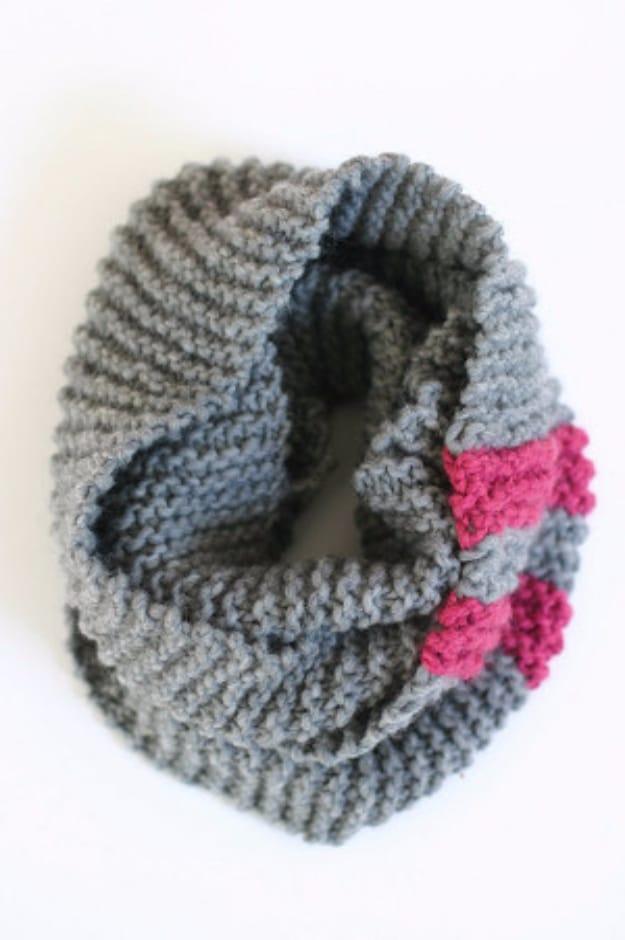 Thick grey garter stitch knitted cowl coiled on a white surface with two blocks of bright pink at one edge
