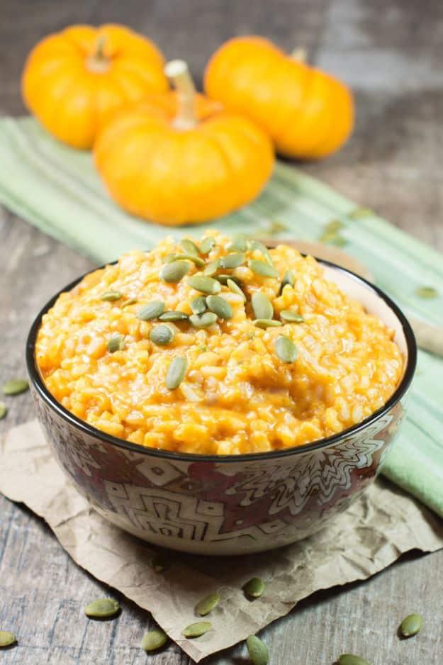 Dark patterned bowl of creamy orange pumpkin risotto topped with green pepitas, mini pumpkins behind