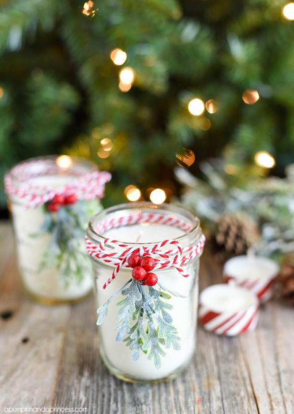 Two small mason jar soy candles tied with red and white baker's twine, frosted greenery and berries in front of a lit tree