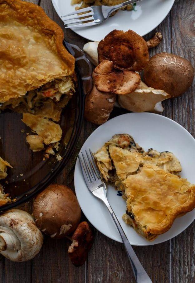 Roasted mushroom pot pie with flaky golden pastry, a slice on a white plate and whole mushrooms beside it