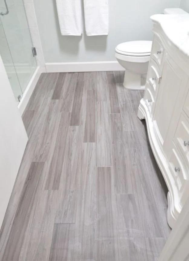 Modern vinyl plank bathroom floor, gray wood look planks in random offset beside a white vanity and glass shower