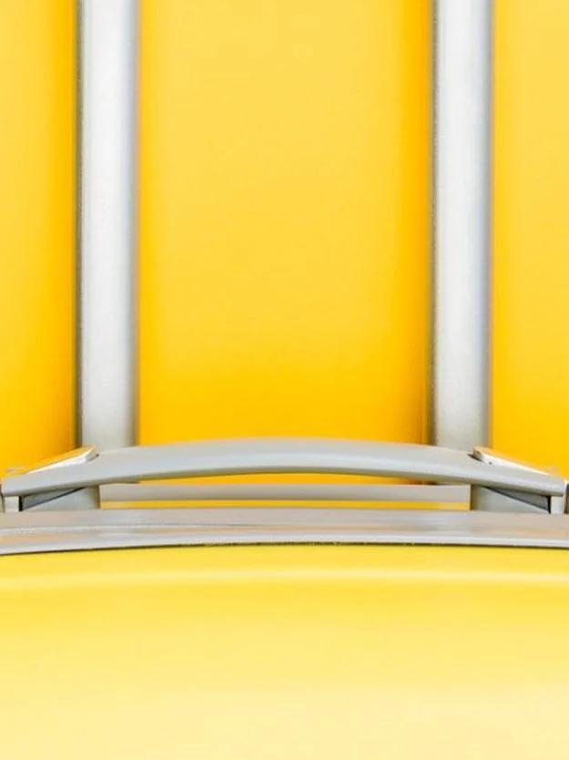 Close crop of a yellow hard shell suitcase and its silver telescoping handle against a bright yellow background