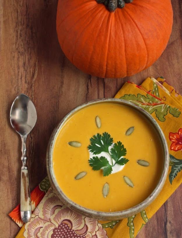 Pumpkin chipotle soup in a grey bowl topped with cilantro and pumpkin seeds beside a whole orange pumpkin