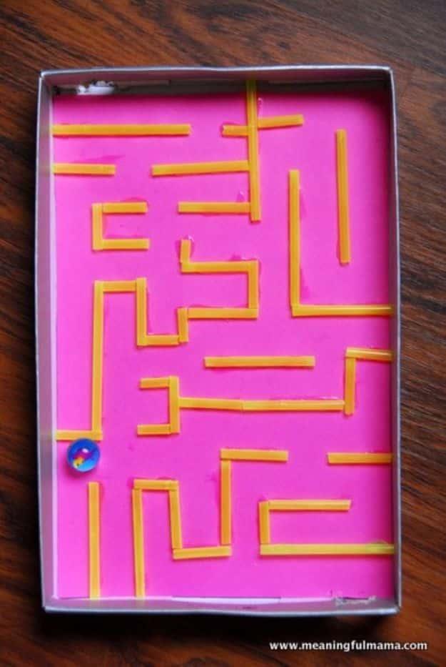 Shoe box lid lined with pink paper and yellow cut straws glued into a maze path, with a marble in one corner